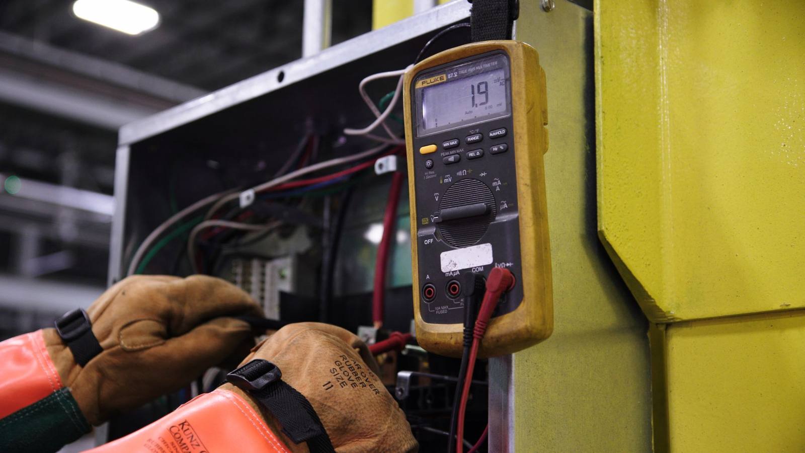 An electrician testing the wiring of an industrial control panel with a multimeter.