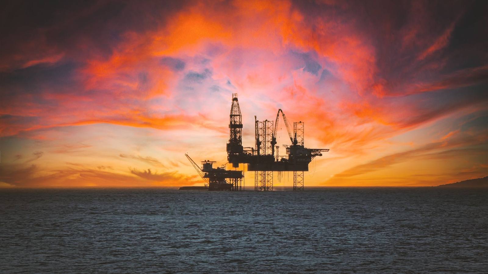 An offshore oil rig silhouetted against a sunset sky with dramatic clouds.