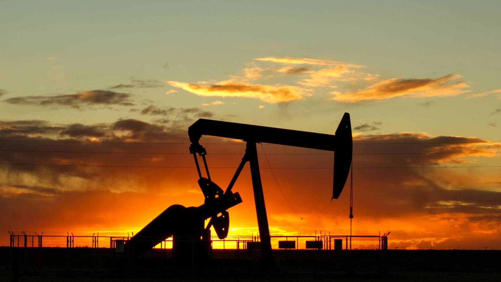 An oil pump jack silhouetted against a colourful sunset sky.