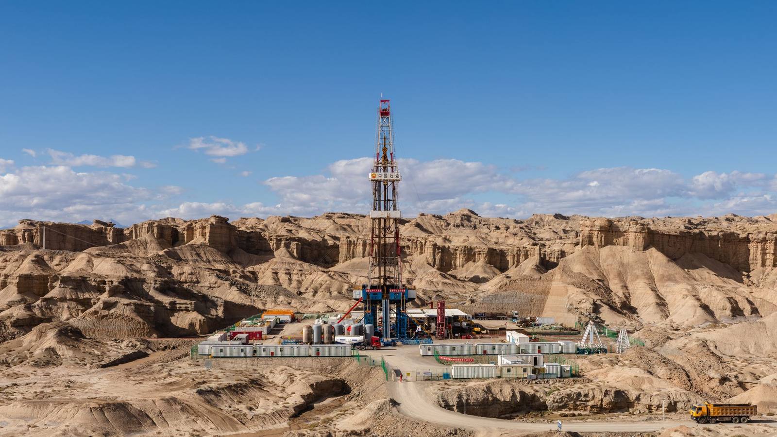 An aerial view of a land drilling rig among barren rock formations and hills.